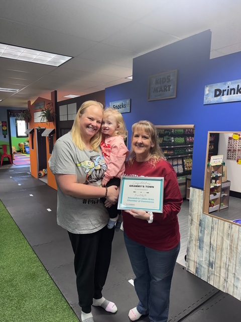 Chris and family in front of the Kids Mart, holding a congratulations certificate from the Alexandria Lakes Area Chamber of Commerce