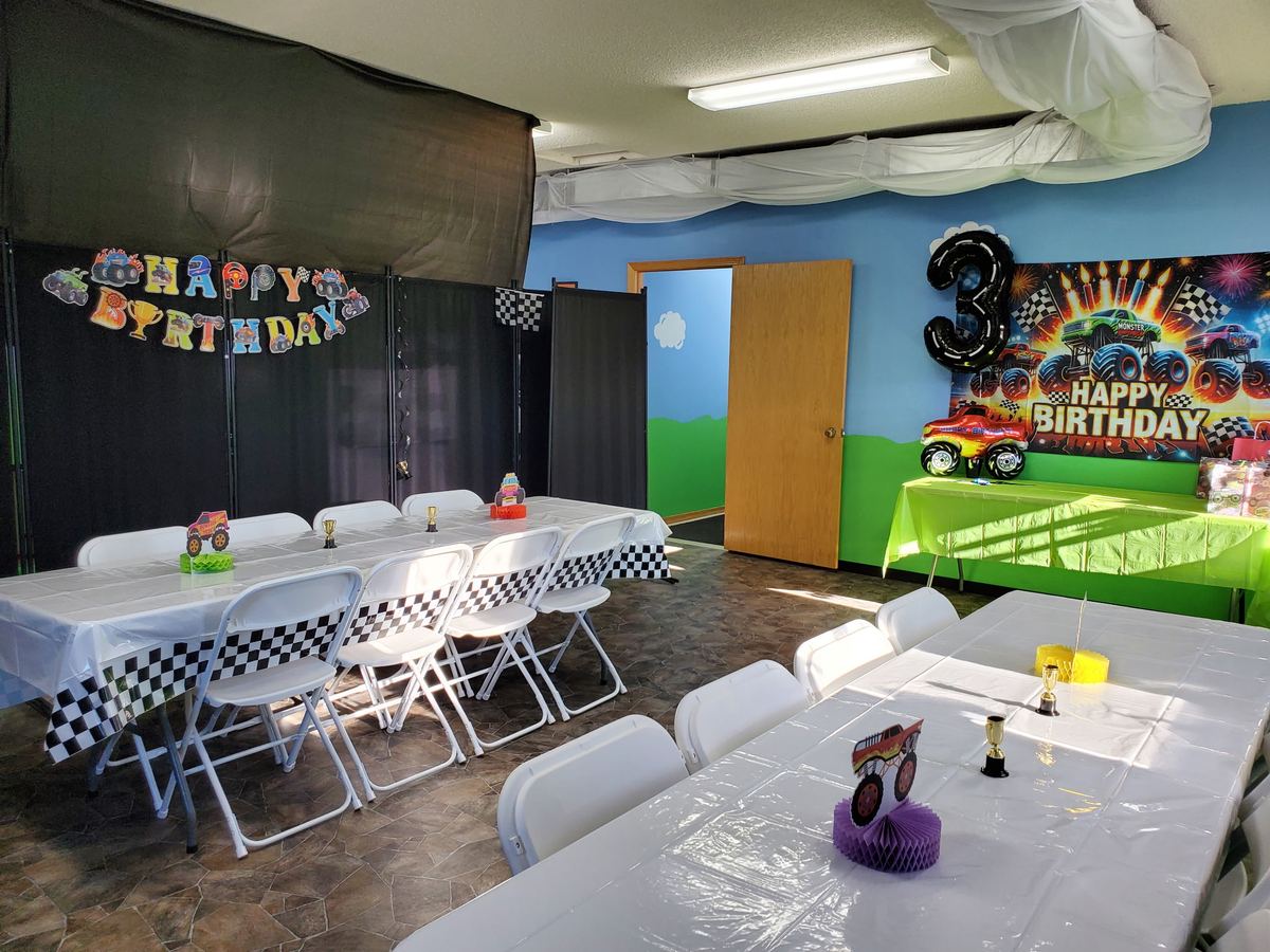 Party room set up for a monster truck third birthday, with checkered tablecloths and trophies